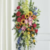 Tall floral standing spray with roses, lilies, sunflowers, and blue accents