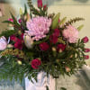 Pink roses and lilies arranged with large pink chrysanthemums in a white vase