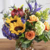 Mixed bouquet with sunflowers, roses, hydrangea, and purple spikes in a glass vase