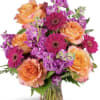 Orange roses and magenta gerbera daisies in a glass vase