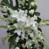 Tall standing spray of white lilies, roses, and other white flowers with large dark tropical leaves.