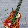 Tall floral arrangement shaped like a guitar with orange mums, red lilies, and white orchids on an easel.