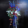 Standing spray of red roses and carnations with blue delphinium and white flowers on an easel