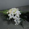 Cascading bouquet of white orchids and ivory roses with dark tropical foliage on a gray surface