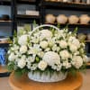 Serene White Sympathy Basket is an elegant and heartfelt floral tribute designed