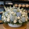 White basket arrangement with blue hydrangeas, white roses, and lilies