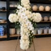 White floral cross arrangement on a stand with roses and orchids