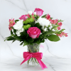 Pink roses and white blooms arranged in a glass vase with a pink ribbon
