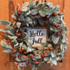Fall wreath with blue-green leaves and berry accents around a Hello Fall sign