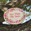 Oval floral sign reading "You Make Me Smile" on a tree branch
