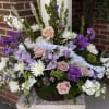 Basket arrangement of pink roses, white daisies, and purple flowers with a ribbon