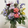 Mixed bouquet of pink roses, lavender blooms, and blue flowers in a glass vase