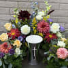 Colorful floral arrangement around a black urn with a cross