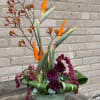 Tall tropical flower arrangement with orange bird-of-paradise blooms in a green container