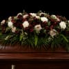 A beautifully composed casket spray designed with rich burgundy blooms, soft ivory