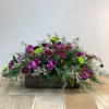 Low floral arrangement in a dark rectangular container with purple and green blooms