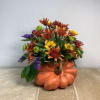 Fall flower arrangement in a pumpkin-shaped container with orange, yellow, and purple blooms