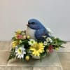 This cheerful spring arrangement features a charming bluebird nestled in a bed