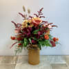 Mixed bouquet in a gold tin vase with orange, burgundy, and yellow flowers
