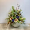 Mixed floral arrangement in a white vase with yellow, purple, and cream blooms