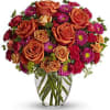 Orange roses and magenta daisies in a clear glass vase