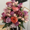 Pink and lavender roses with lilies in a black hatbox, topped with a graduation cap.