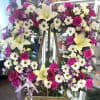 Large floral wreath on an easel with white lilies, daisies, roses, and purple blooms