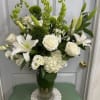 White lilies, roses, and green blooms arranged in a clear glass vase.