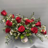 Red roses arranged in a low white vase with small white filler flowers