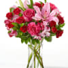 Bouquet of pink lilies, red roses, and carnations in a clear glass vase