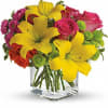 Bouquet of yellow lilies, pink roses, and green button mums in a clear square vase