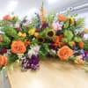 Large mixed floral arrangement with orange roses, sunflowers, and lilies on a table