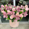 Pink roses and orchids arranged in a blush hatbox