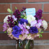 Round vase arrangement with purple, pink, and white flowers in a clear vase with branches inside