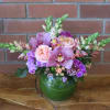 Pink and purple flowers arranged in a green glass vase