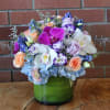 Mixed bouquet of orchids, roses, and hydrangeas in a green glass vase