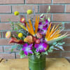 Tropical arrangement with orange birds of paradise, purple orchids, and calla lilies in a green-lined glass vase