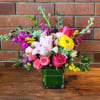Bright mixed bouquet of pink roses and yellow ranunculus in a square glass vase lined with green leaves