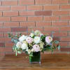 Low arrangement of white and pale pink flowers in a square glass vase lined with green inside