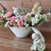Pink and white floral arrangement in a white bowl with angel figurines