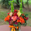 Bright orange and pink rose arrangement with yellow calla lilies and tall green bells of Ireland in a glass vase