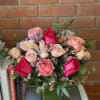 Rounded arrangement of pink and cream roses with tiny pink blossoms in a square glass vase