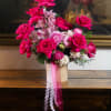 Hot pink roses and pale pink orchids in a beige vase with ribbon tails
