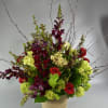 Tall floral arrangement with red roses, purple blooms, and green hydrangeas in a burlap-wrapped vase