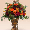 Mixed bouquet of orange, red, and pink flowers in a bronze urn vase