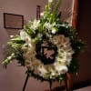 White floral wreath on a black easel with lilies and daisies