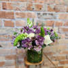Purple and white bouquet in a glass vase on a wooden base