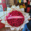 Round bouquet of red roses wrapped in white paper with a pink ribbon