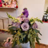 Lavender roses and purple flowers arranged in a glass vase