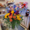 Bouquet of sunflowers, orange roses, and blue delphinium in a glass vase